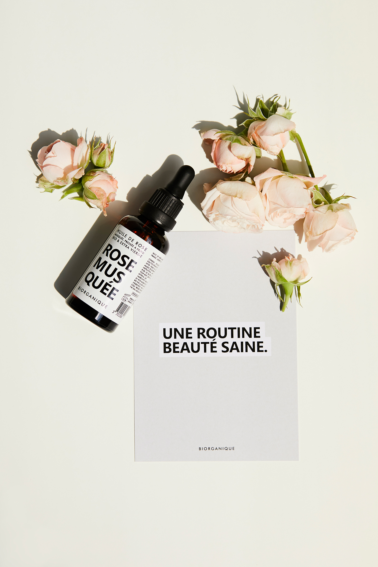 Butelka z olejem Biorganique France leżąca w słońcu na jasnym tle z różami